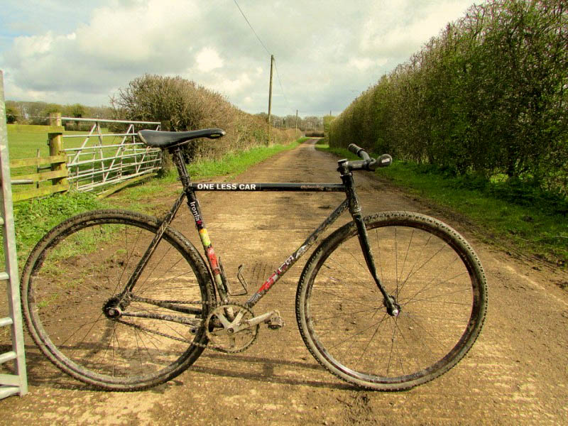 Right profile of a Surly Steamroller bike, black, parked in the middle of a gravel road in the country
