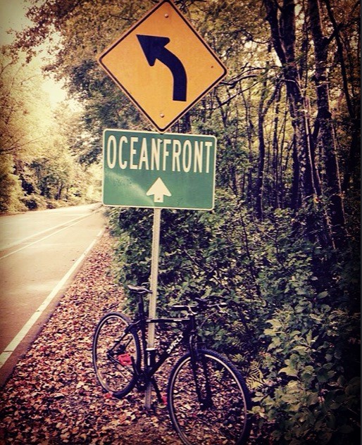 Front, right side view of a black Surly bike, parked on a roadside, in front of a sign pointing to Oceanfront