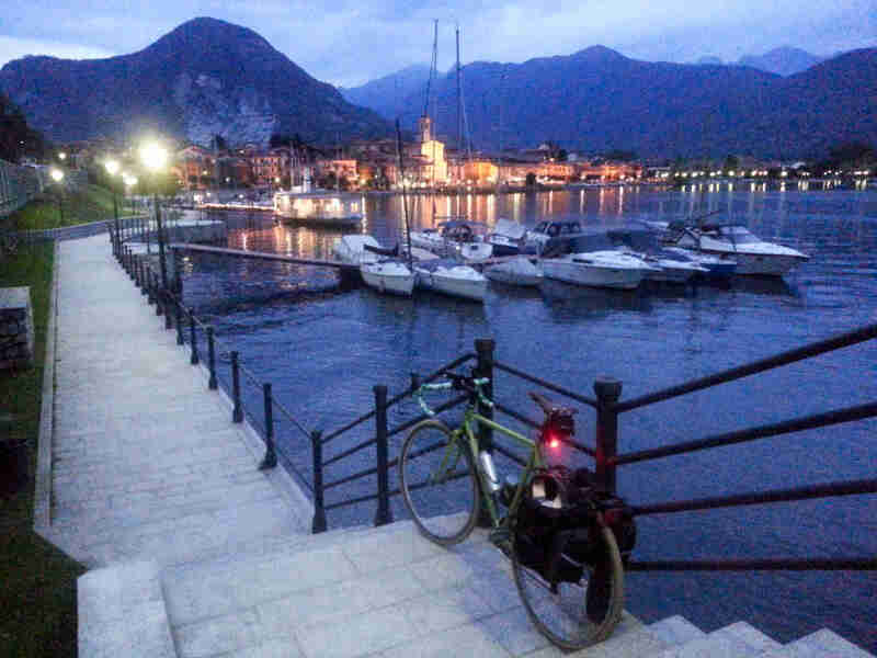 Rear view of a green bike parked on a set of stairs, along the handrail, with boats in a bay and mountains in background