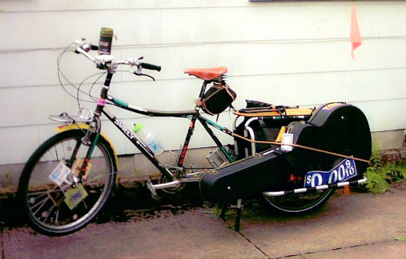 Left side view of a Surly Big Dummy bike with guitar on the back left side, parked along a wall of a house