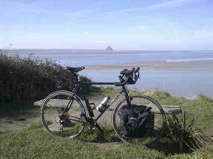 Right side view of a forest green Surly Cross Check bike, parked against a bench, with a body of water in the background