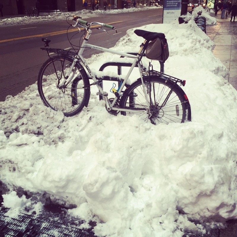Left side view of a white Surly Long Haul Trucker with racks, parked on a snowbank on the side of a city street