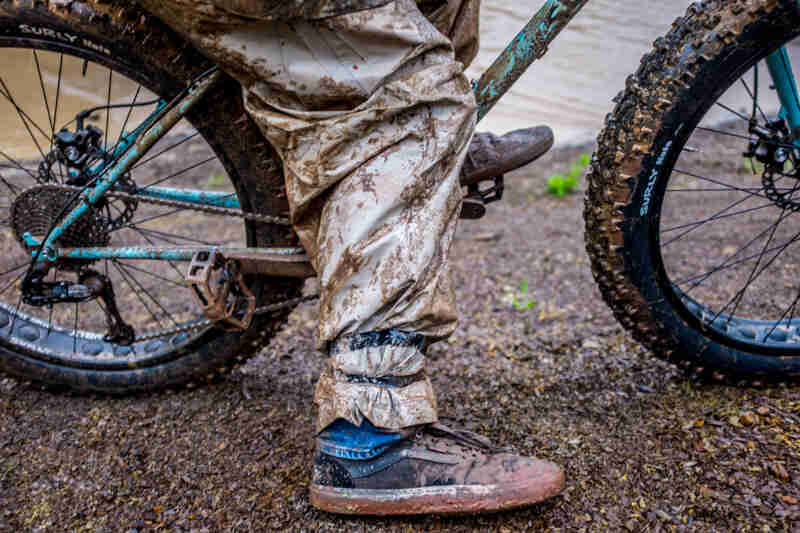 Cropped lower-half view of a cyclist on a dirty fat bike, covered in muddy clothing