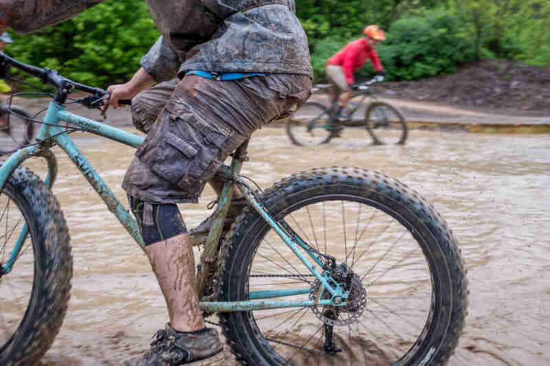 Left side cropped view of the lower half of a cyclists riding a Surly fat bike across muddy water