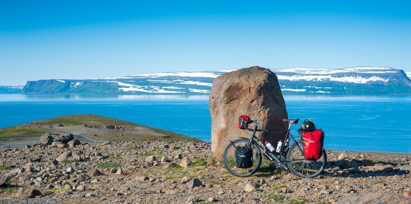 Left side view of a black Surly Long Haul Trucker bike, on a rocky field in front of a boulder, with icy blue waters