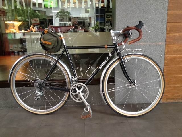 Right side view of a black Surly bike, parked against a glass wall, on the outside of a retail store