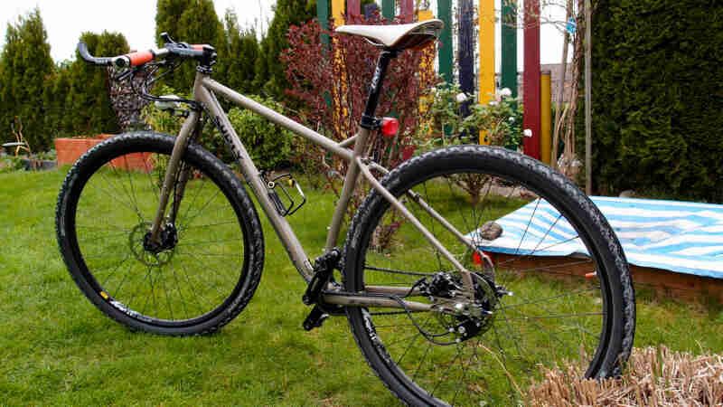 Right side view of a tan Surly bike, parked in a backyard, with hedges in the background