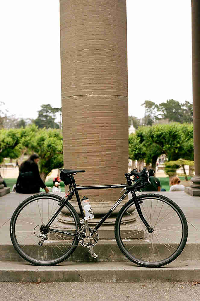 Right side view of a black Surly Cross Check bike, parked on a stair in front of a large, concrete pillar