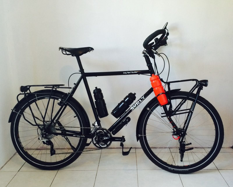 Right profile of a Surly Long Haul Trucker bike, black, parked in tile against a white wall in a room