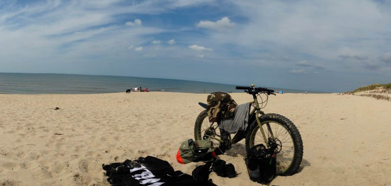 Front right view of a Surly fat bike, parked on a sandy beach, with the ocean in the background