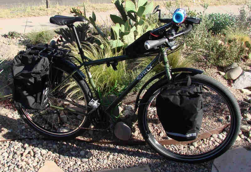 Right side view of a green Surly Ogre bike, parked on gravel, in front of a landscaped plot with grasses and cacti