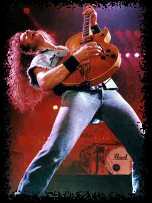 Front view of musician, Ted Nugent, standing and leaning back, playing a guitar on a stage