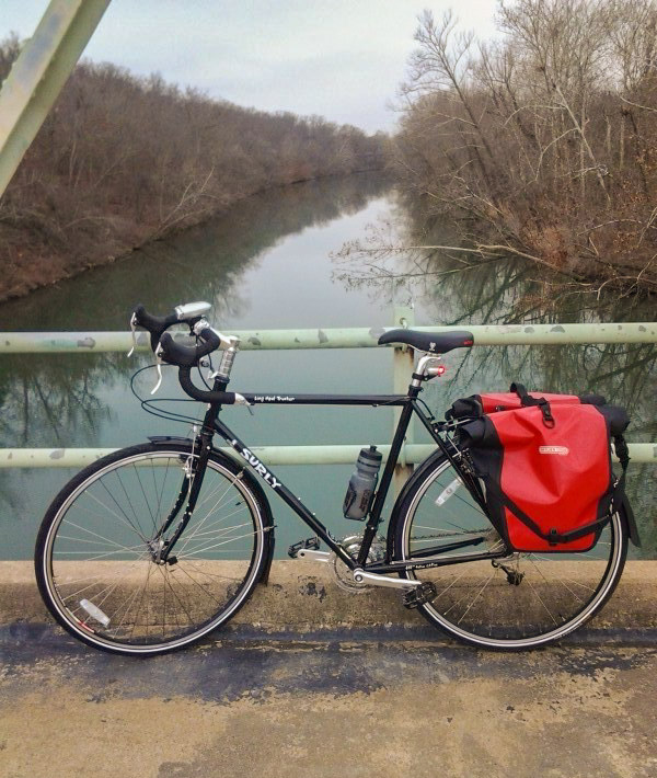 Right side view of a Surly Long Haul Trucker bike, black, parked along the rail on a bridge over a river, in the fall