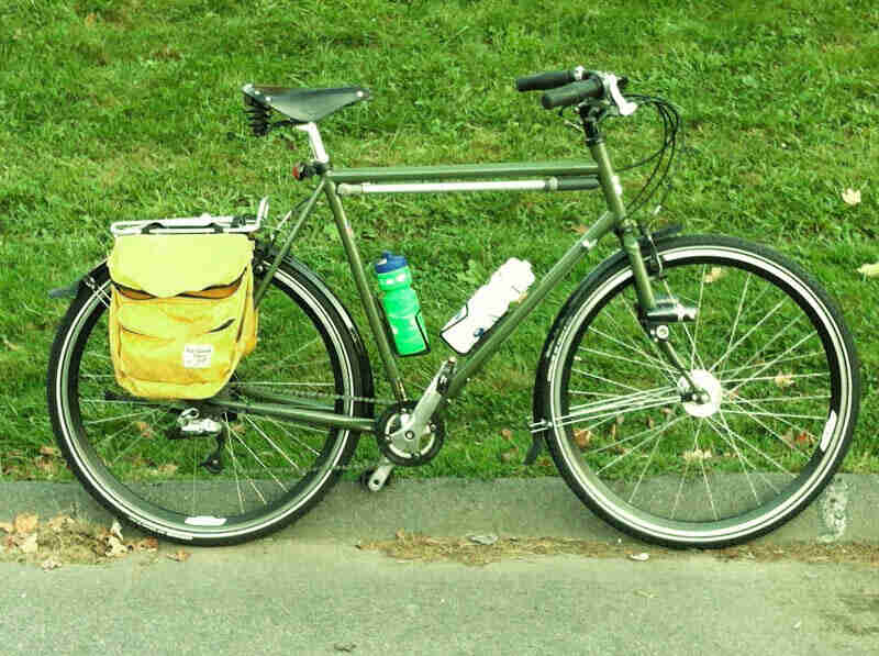 Right side view of a green Surly bike with yellow rear saddlebags, parked against the curb in front of a grass hill