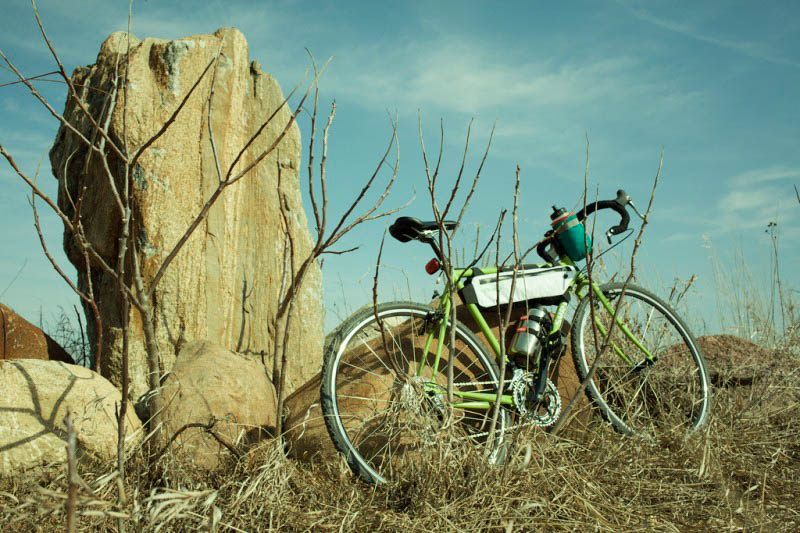 Right side view of a lime green Surly bike, parked in brush next to a boulders