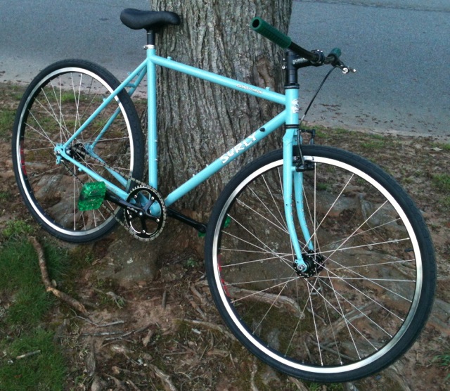 Right side view of a turquoise Surly Cross Check bike, parked on roots at the base of a tree