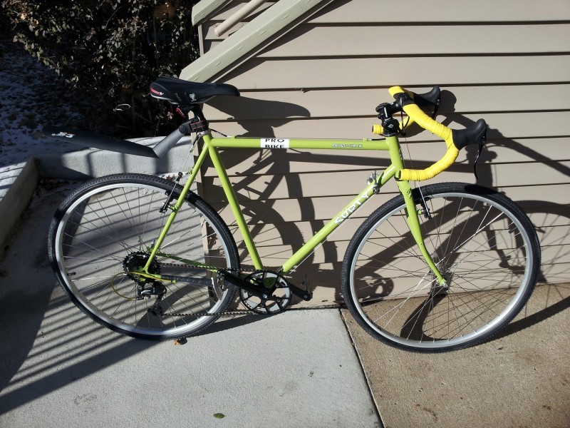 Right side view of a lime green Surly Cross Check bike, leaning on the outside of a wall, from a set of stairs