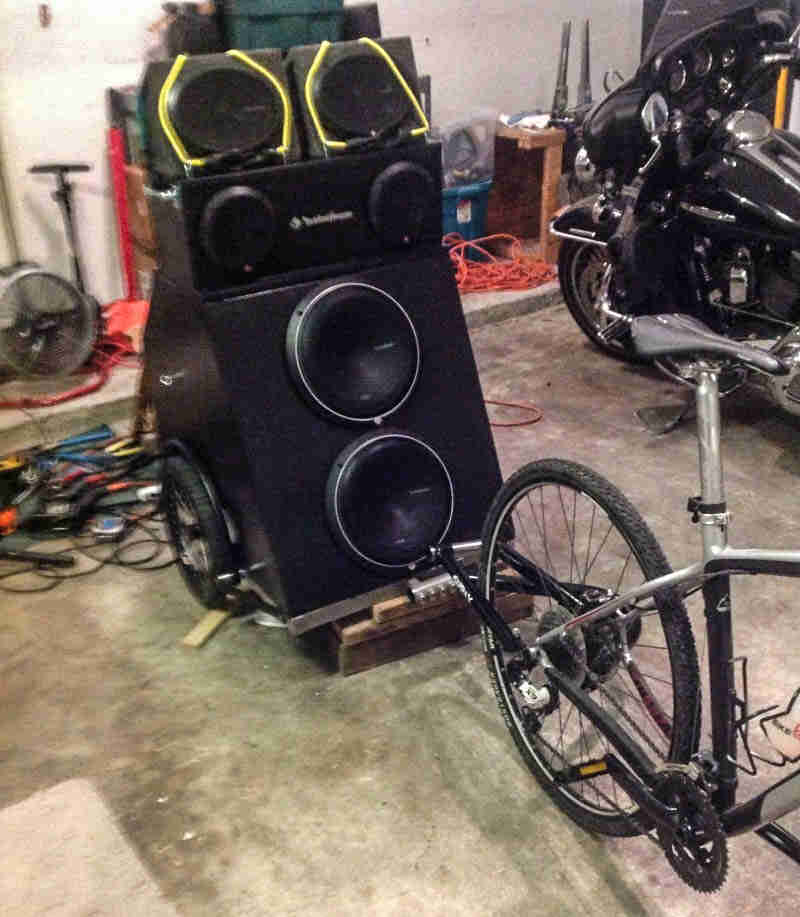 A bike trailer of speakers, mounted to the rear of a bike, parked in a garage next to a motorcycle