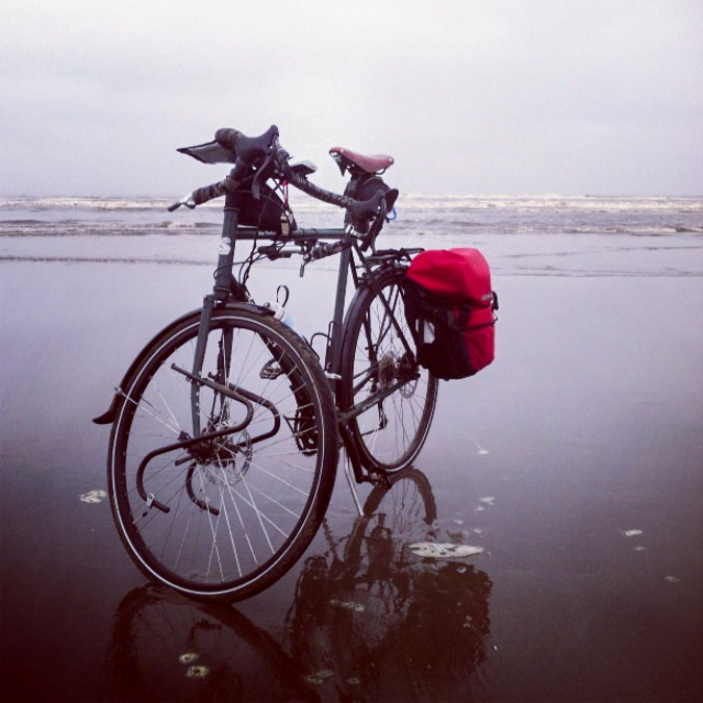 Front view of a Surly bike, parked in wet sand on a seashore, with ocean waves in the background