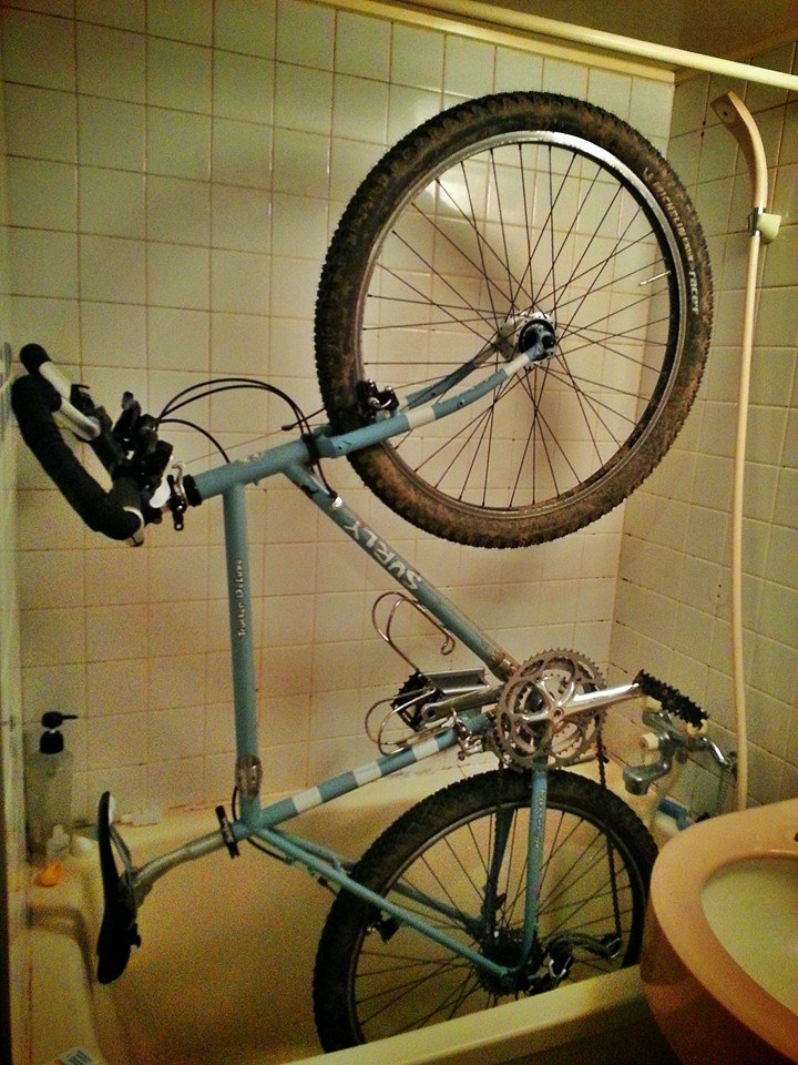Right side view of a light blue Surly Long Haul Trucker bike, standing up vertically, inside of the tub in a bathroom