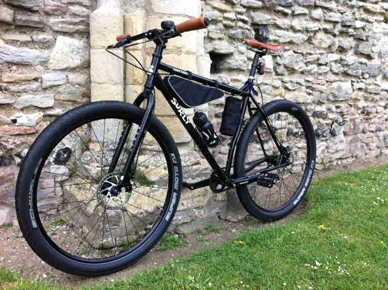 Left side view of a black Surly Karate Monkey bike, leaning against a stone wall
