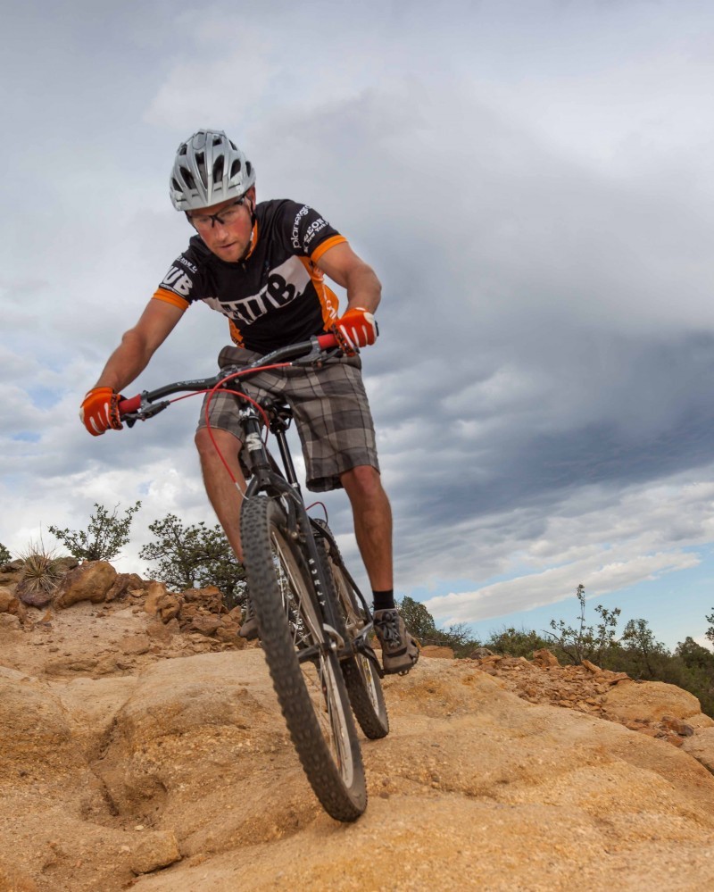 Front view of a cyclist, riding a black Surly bike down a boulder hill