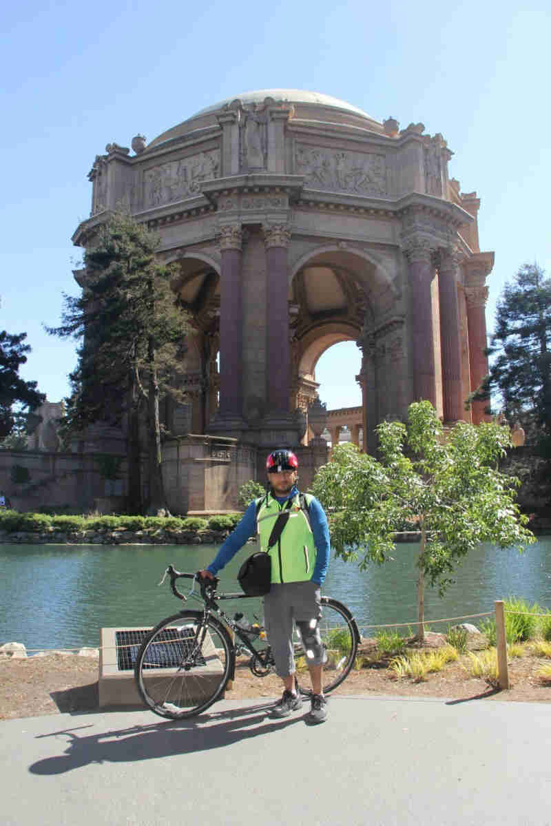 Left side view of a black Surly Cross Check bike with a cyclist standing in front, and a stone structure behind them