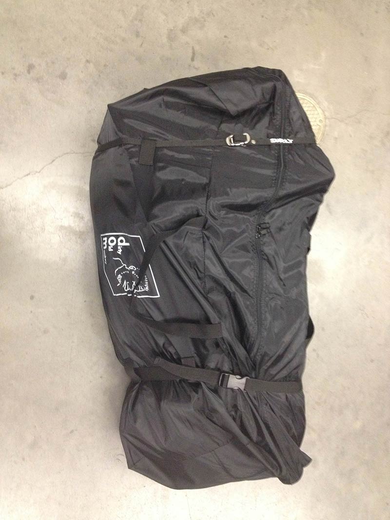 Downward view of a zipped up, black gear bag, with a Surly Junk Strap wrapped around it, on a cement floor