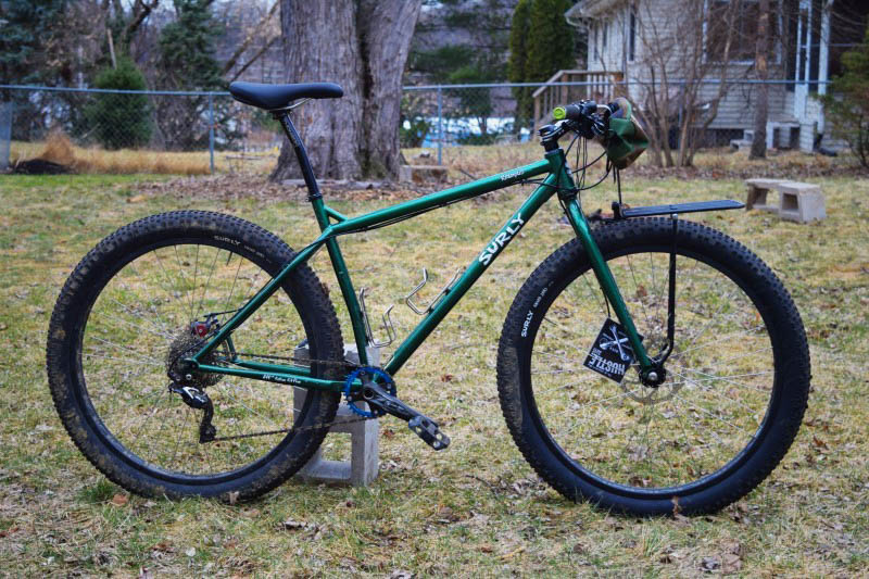 Right profile of a Surly Krampus bike, green, parked on the grass in a yard, with a house in the background