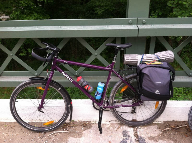 Left side view of a purple Surly Troll bike, parked on the side of a bridge next to the rail
