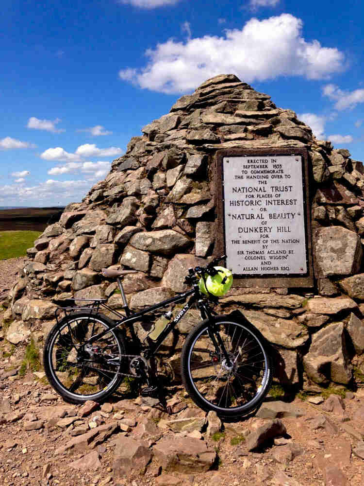 Right side view of a black Surly Troll bike, parked against a Dunkery Hill monument, constructed on stacked stones