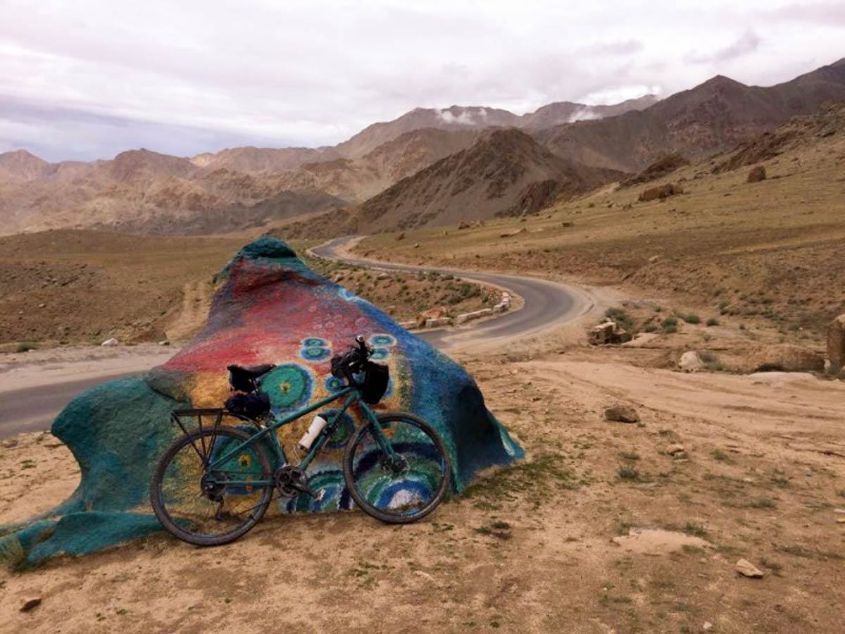 Right side view of a green Surly Troll bike with gear, parked against a painted rock, with mountains in the background