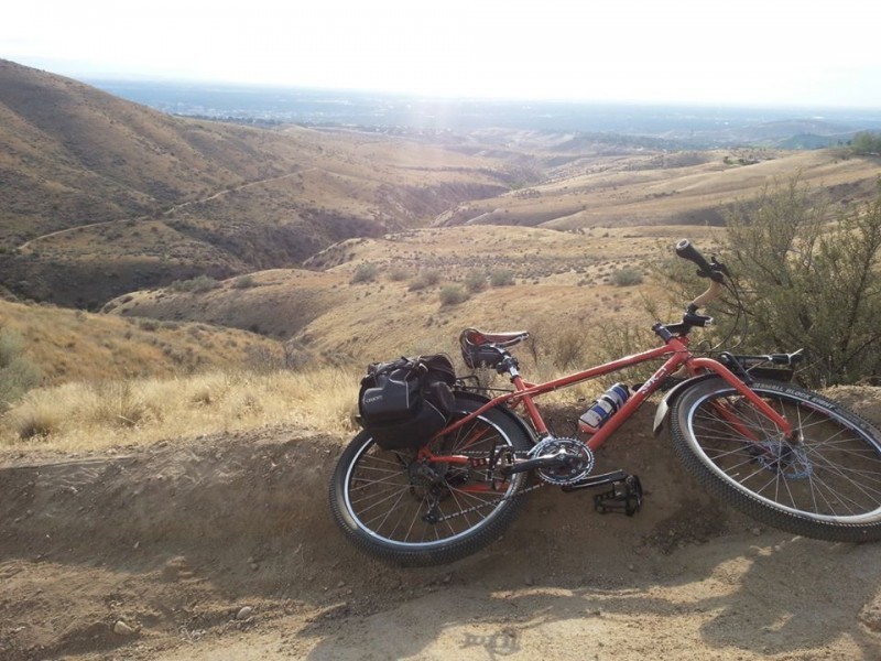 Right side view of red Surly Troll bike with gear, laying on a dirt bank, with brown, grassy hills in the background