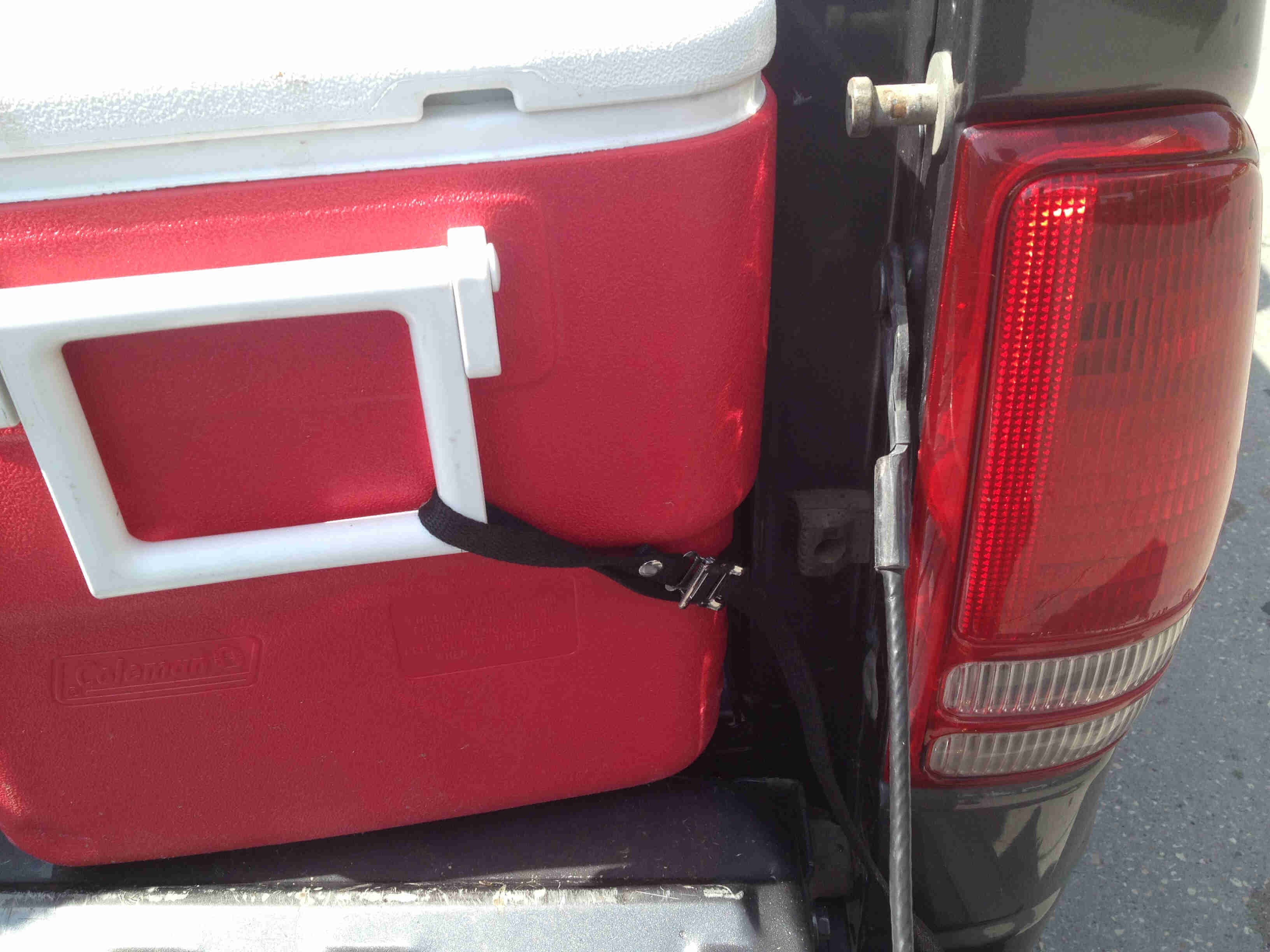 Close up view of a red cooler, strapped into a pickup truck bed, using a Surly Junk Strap