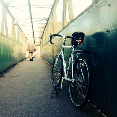 Rear, left side view of a Surly bike, leaning on a wall in a skywalk, with a person walking away ahead