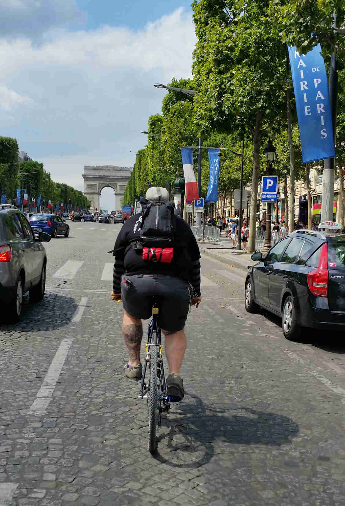 Rear view of a cyclist riding their Surly bike on a street with cars, towards the Arc de Triomphe in Paris