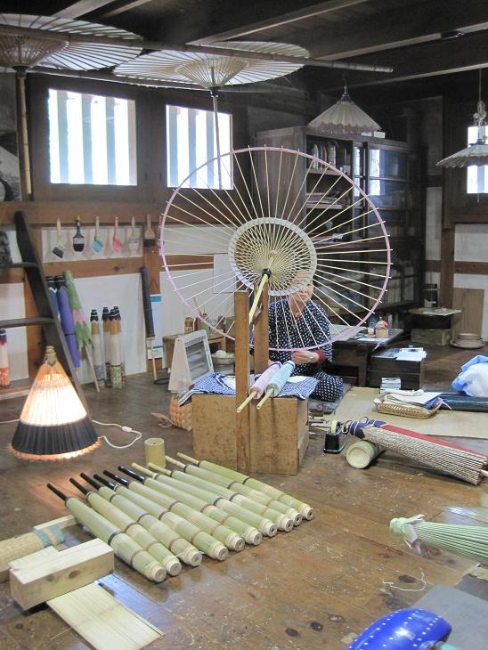 A view inside a handmade umbrella workshop, with a person sitting on the floor and working on one of them
