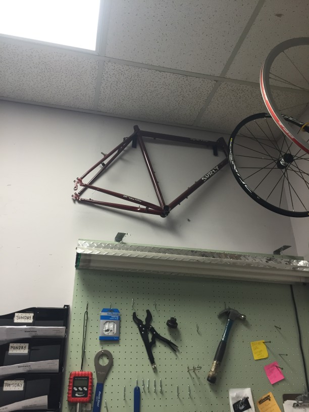 Upward view of a red Surly bike frame, hanging from a rack on a wall, above a shop light