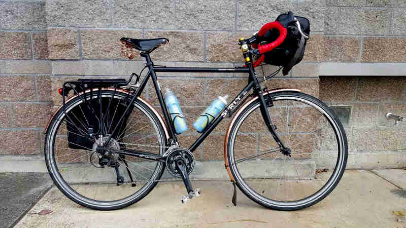 Right side view of a black Surly bike, parked on a sidewalk, in front of a stone block building