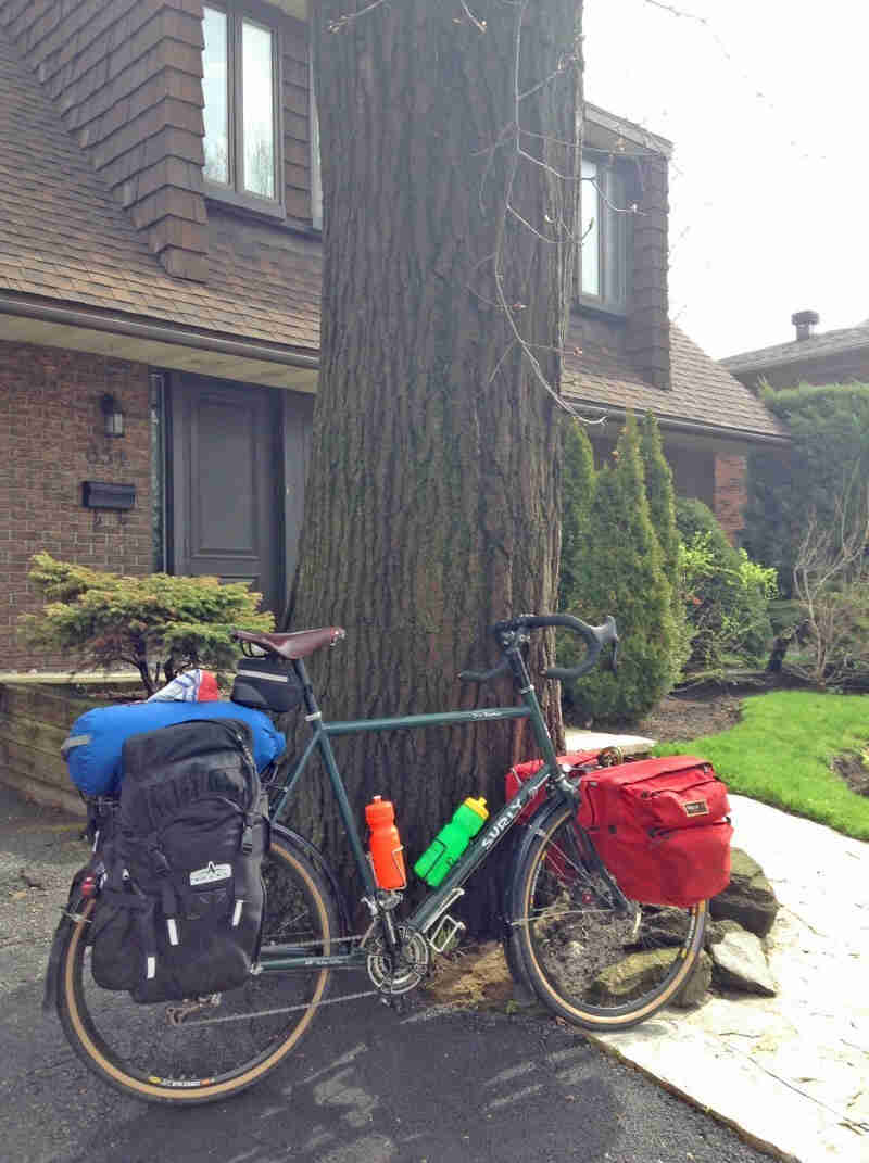 Right side view of green Surly Disc Trucker bike, loaded with gear, parked at the base of a street in front of a house