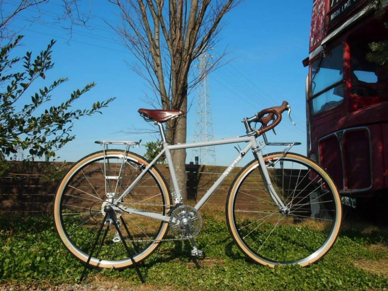Right side view of Surly Cross Check bike, on grass in front of a tree, and a double decker bus to the right