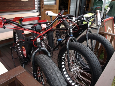 Front, right side view of 3 Surly fat bikes, parked side by side, on a deck outside of a bike shop