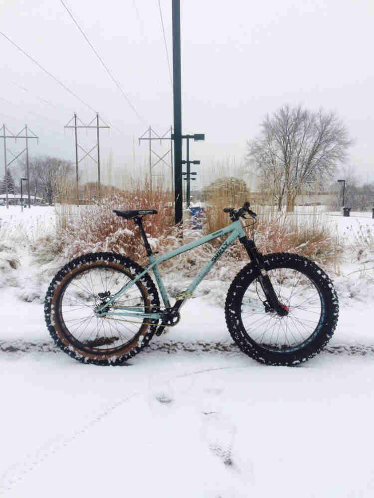 Right profile of a mint Surly Wednesday fat bike, in a snow covered field, with power lines above