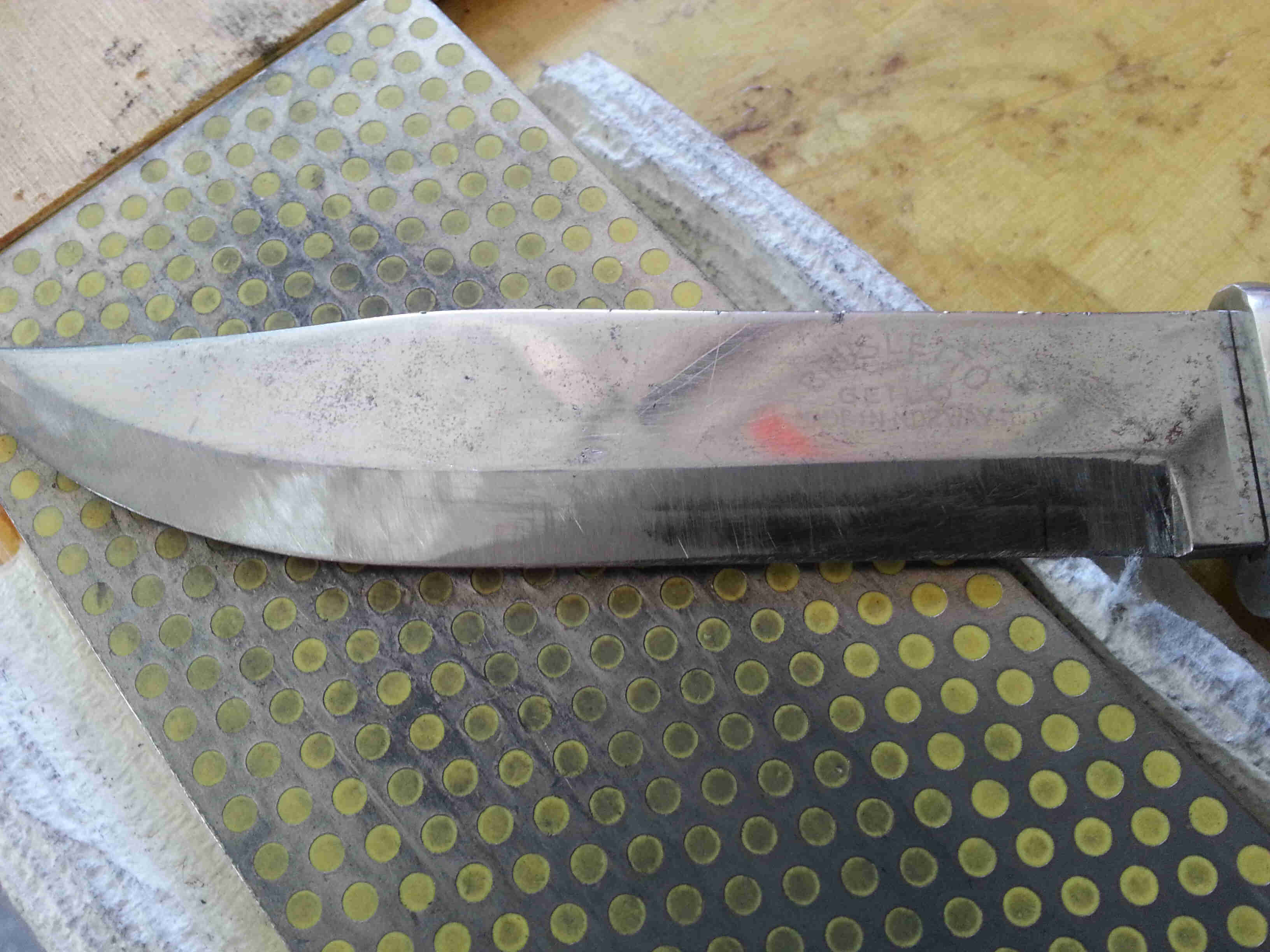 Downward view of a silver knife blade, laying across a sharpening stone