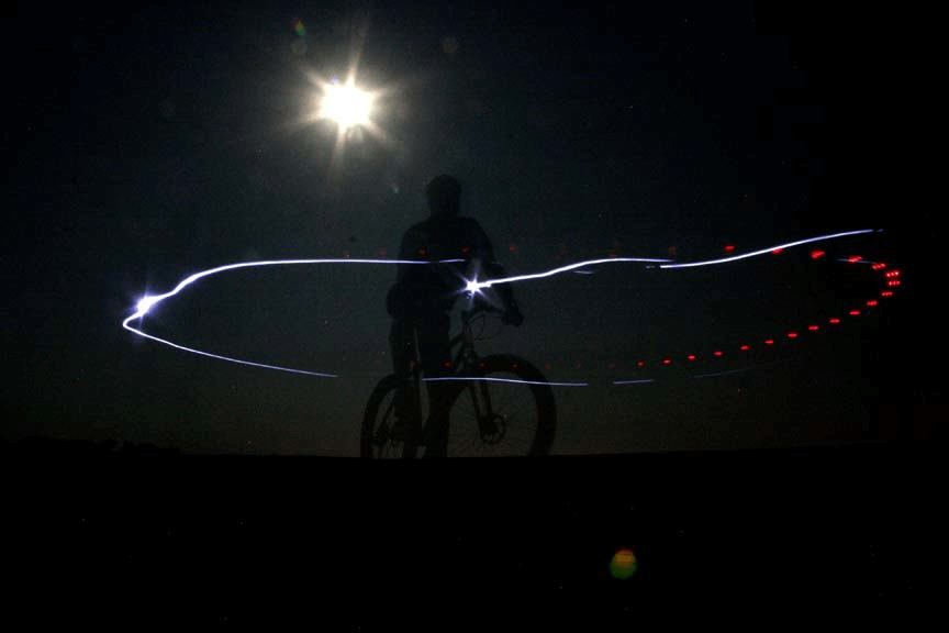 Nighttime, front, right side view of a cyclist on a bike, with a light ring around them - created from the headlight
